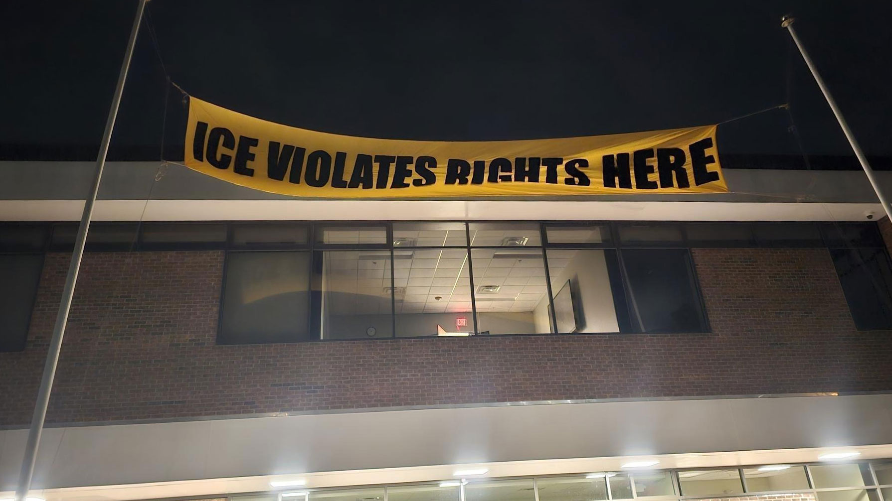 A sign placed on flag poles outside an ICE surveillance center, reading: ICE Violates Rights Here